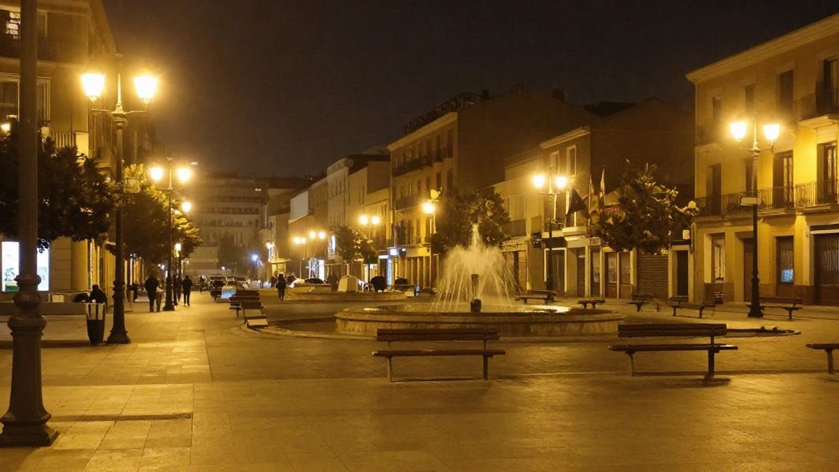 Imagen ilustrativa: calle urbana de noche con luz artificial de farolas y una fuente pública