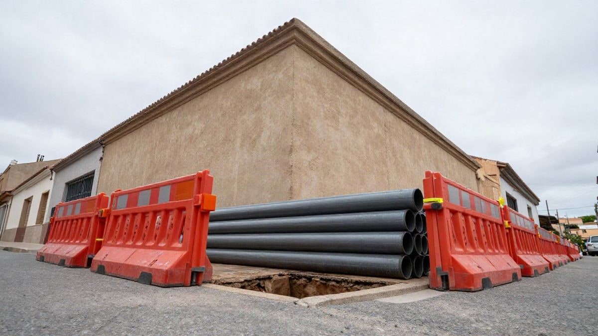 Imagen ilustrativa: zanja abierta con barreras y tuberías en una calle residencial bajo un cielo nublado