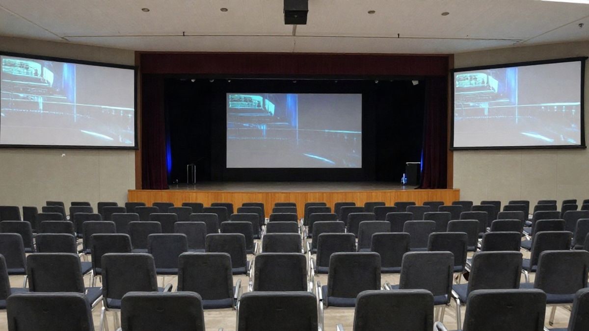 Imagen ilustrativa: interior de un centro de convenciones con butacas vacías y pantallas digitales