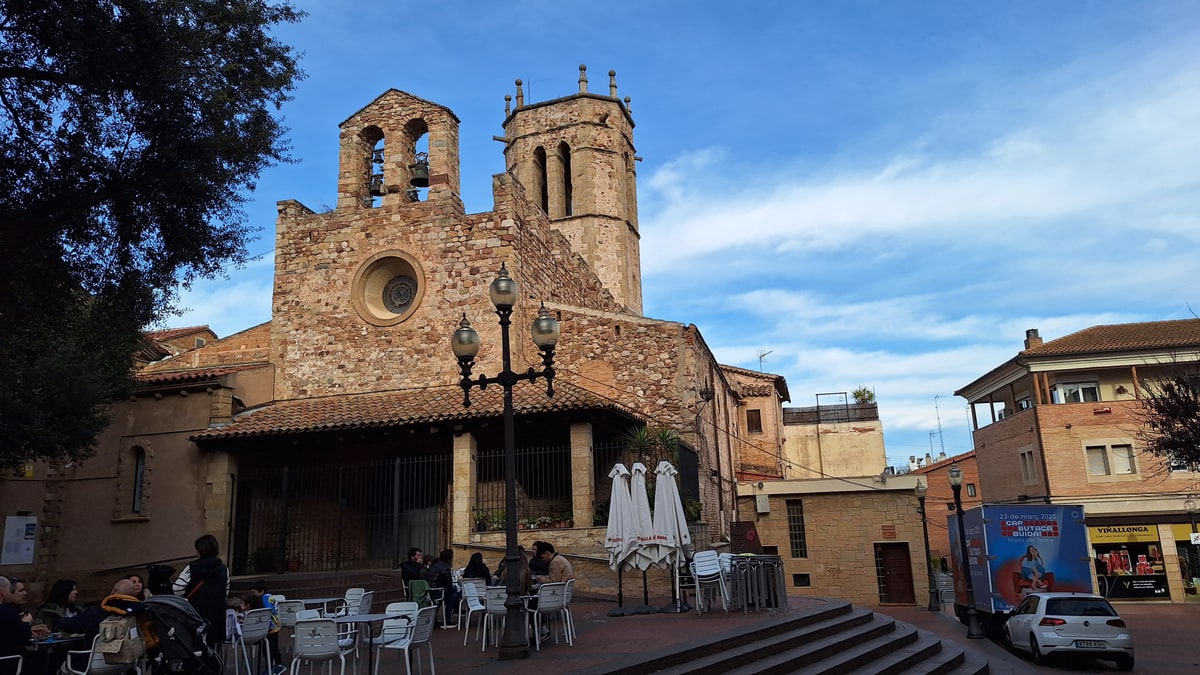 Iglesia medieval de piedra con campanario y terraza en una plaza del centro urbano