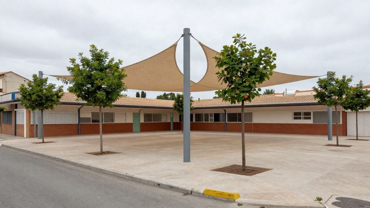 Imagen ilustrativa: patio de una escuela con toldos de sombra y árboles jóvenes, vacío durante las vacaciones.