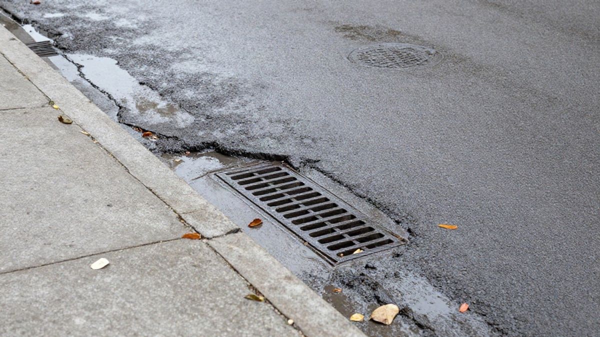 Imagen ilustrativa: detalle de una alcantarilla saturada y asfalto mojado en una calle residencial