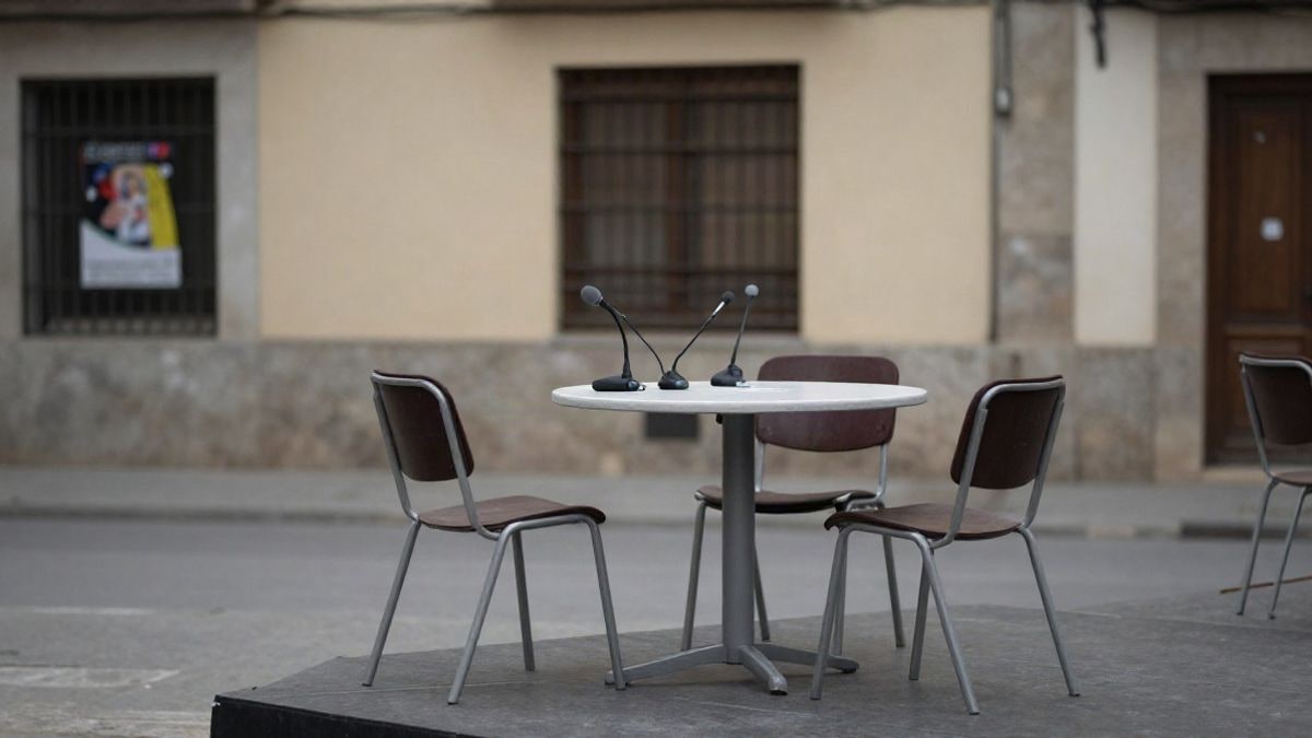 Imagen ilustrativa: una mesa redonda con micrófonos en una sala de actos vacía y luz tenue.