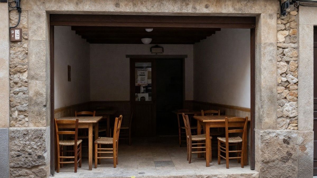 Imagen ilustrativa: interior vacío de un restaurante rústico de piedra y madera con mesas y sillas, visto a través de un ventanal desde la calle.