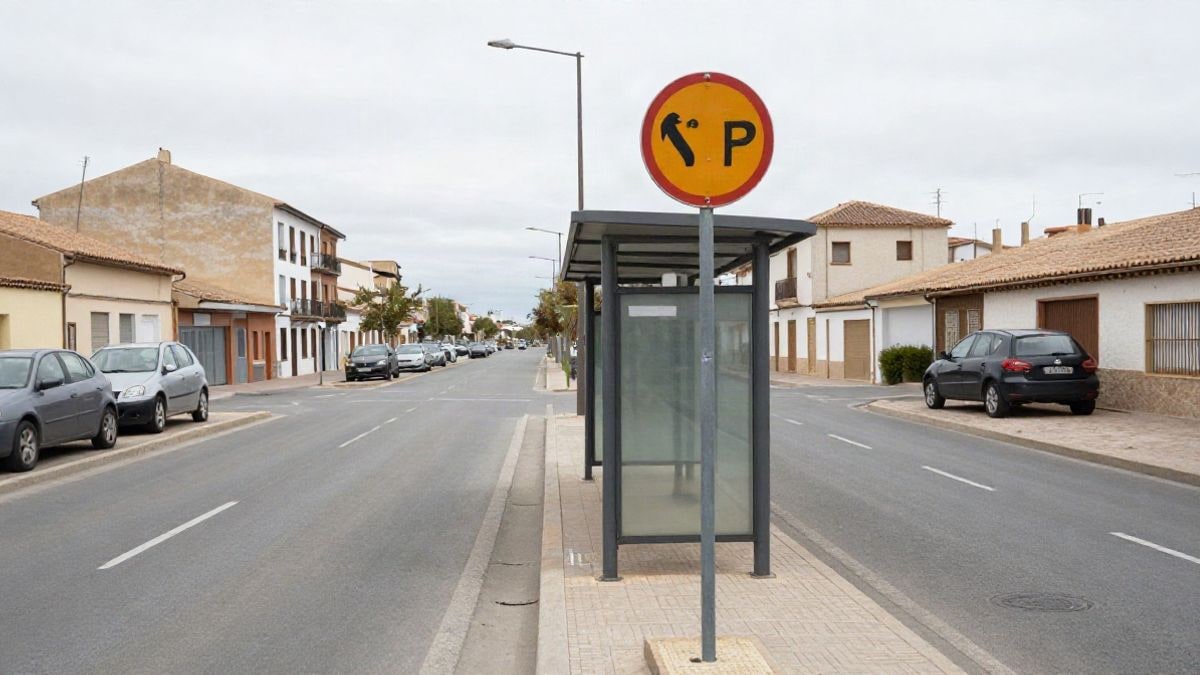 Imagen ilustrativa: marquesina de autobús en una avenida de un pueblo, con señal de parada y edificios de fondo