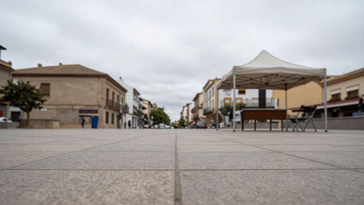 Imagen ilustrativa: plaza pública con una carpa informativa y sillas plegables bajo un cielo nublado