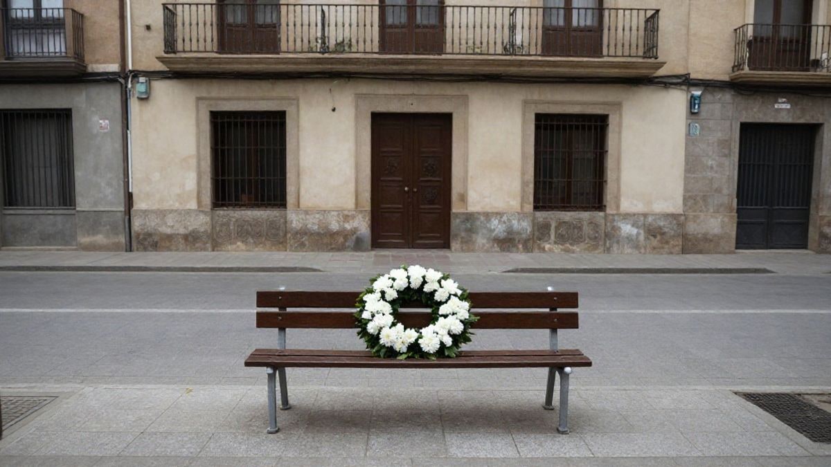 Imagen ilustrativa: corona de flores blancas sobre un banco de madera junto a un edificio institucional genérico