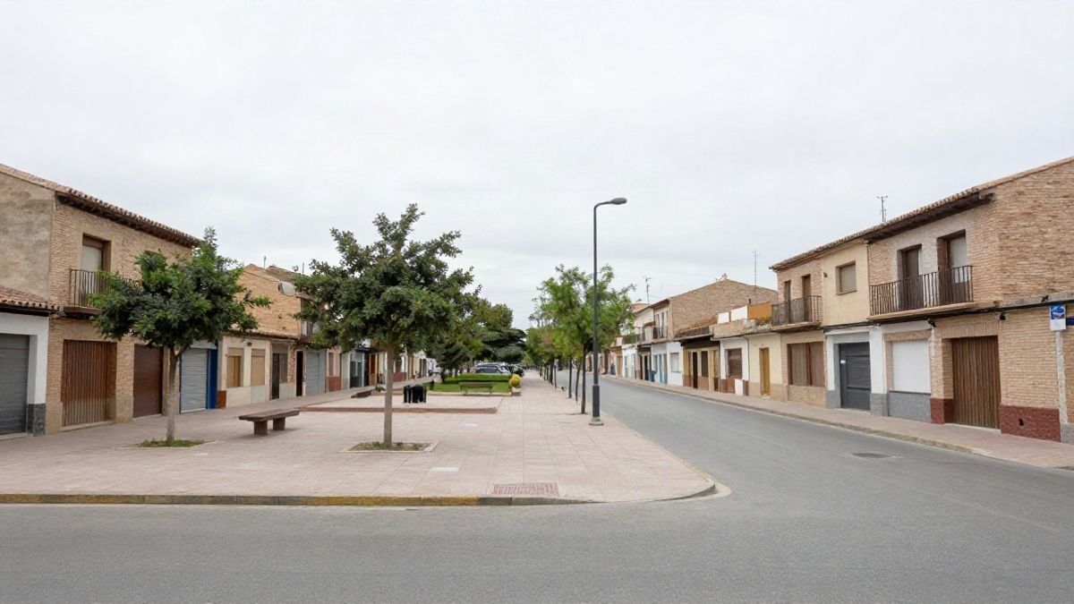 Imagen ilustrativa: una calle tranquila de un barrio residencial con edificios bajos y una pequeña plaza con árboles