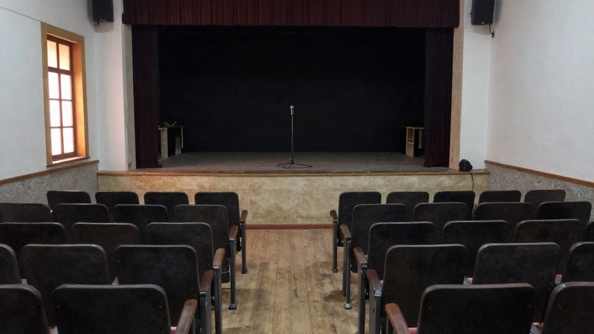 Imagen ilustrativa: interior de una sala de conciertos pequeña con butacas vacías y un micrófono en el escenario