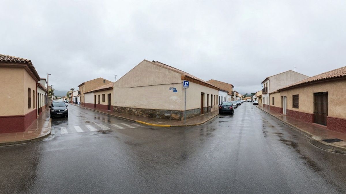 Imagen ilustrativa: calle mojada de un municipio español tras las lluvias intensas, con coches aparcados y edificios bajos al fondo