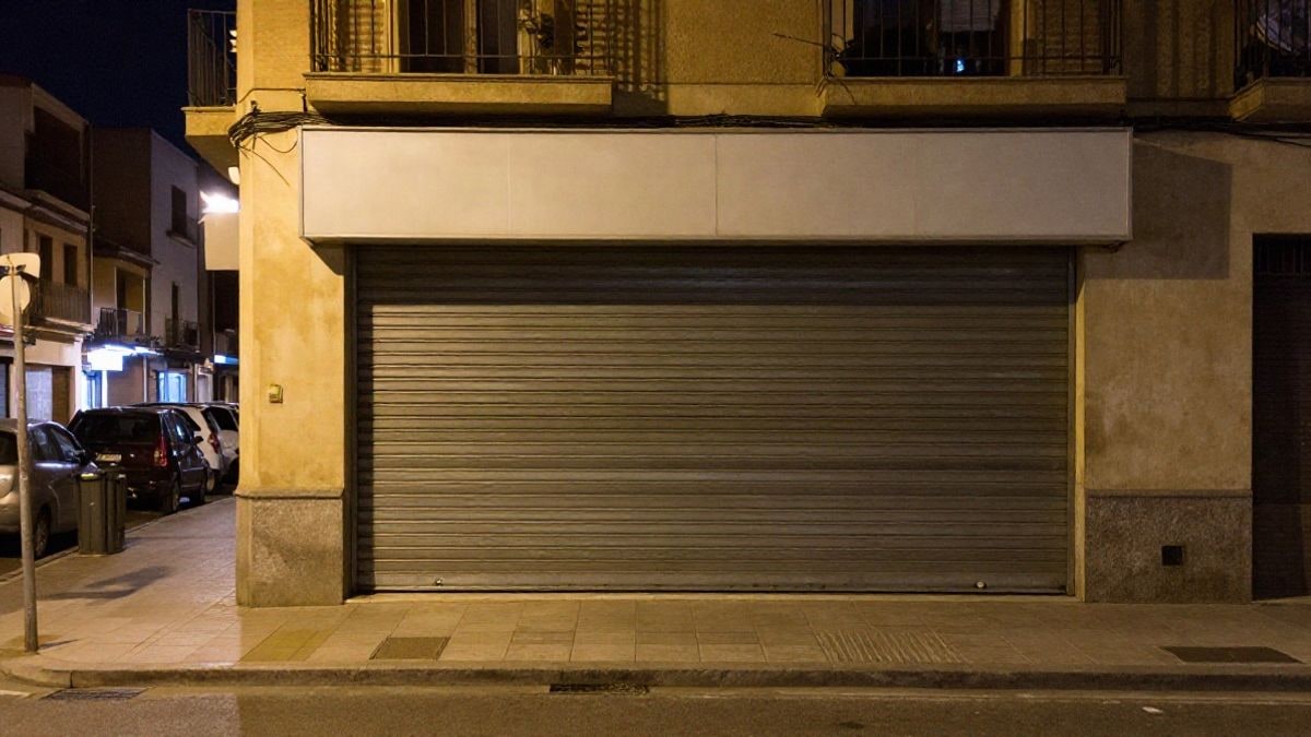 Imagen ilustrativa: fachada de un supermercado genérico con la persiana bajada por la noche en una calle española.