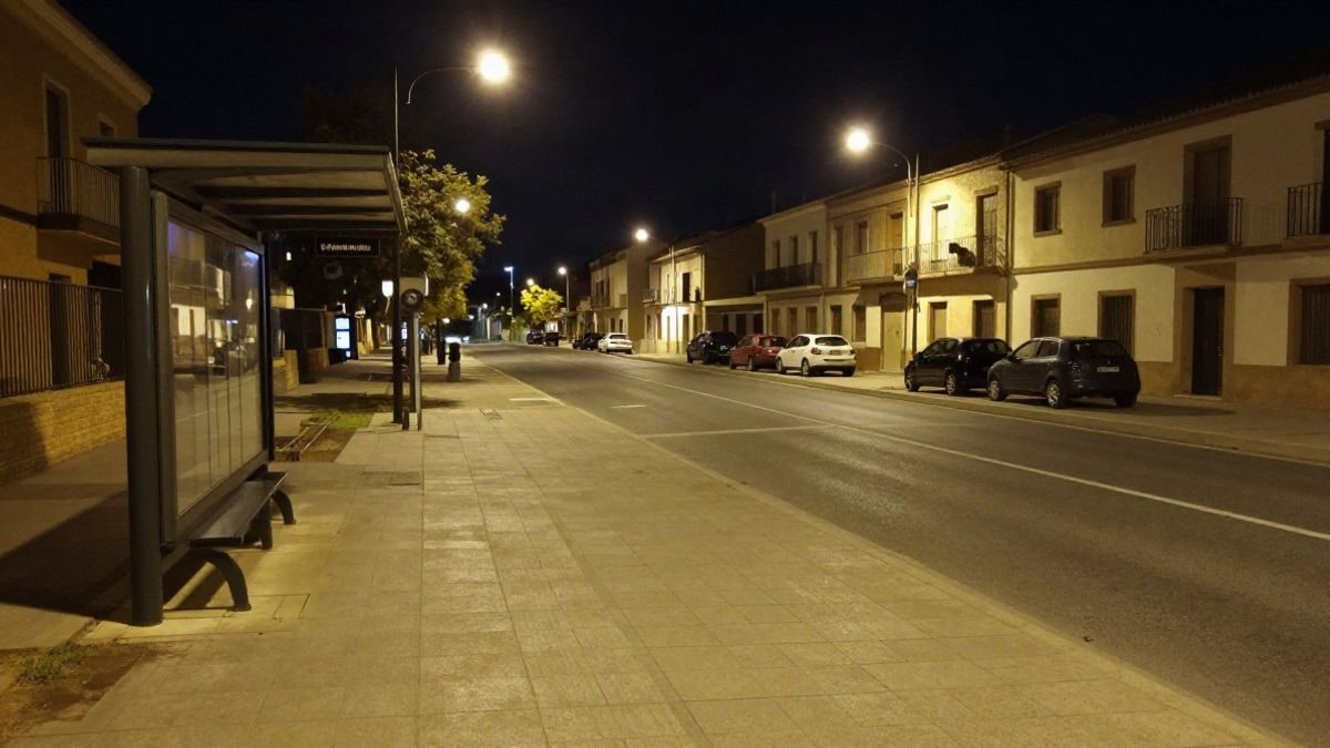 Imagen ilustrativa: una parada de autobús iluminada por farolas en una avenida residencial durante la noche