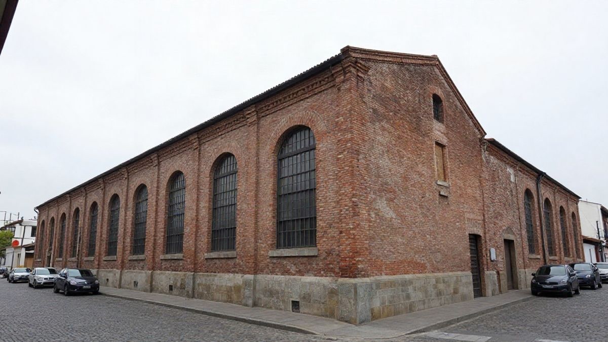 Imagen ilustrativa: fachada de ladrillo visto de un antiguo edificio industrial con arcos, bajo un cielo nublado