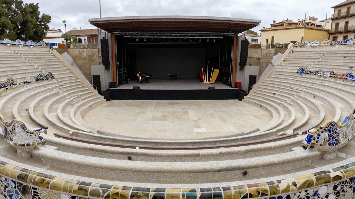 Imagen ilustrativa: escenario al aire libre en un parque modernista con bancos de mosaico y elementos escénicos, sin personas.