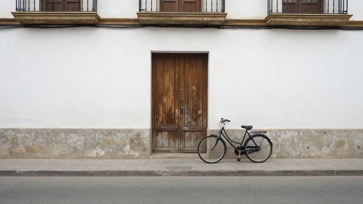 Imagen ilustrativa: fachada sencilla de un edificio cívico con una puerta de madera y una bicicleta apoyada en una barandilla