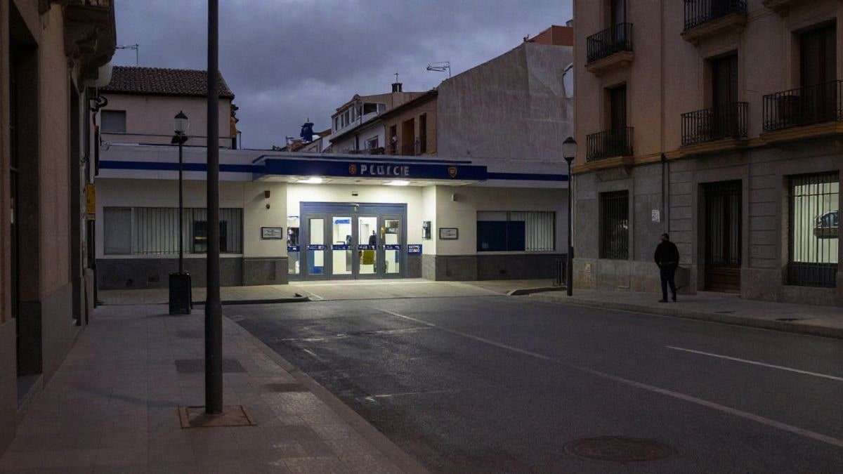 Imagen ilustrativa: una calle nocturna con la entrada de una comisaría de policía municipal iluminada por farolas y un letrero de neón tenue.