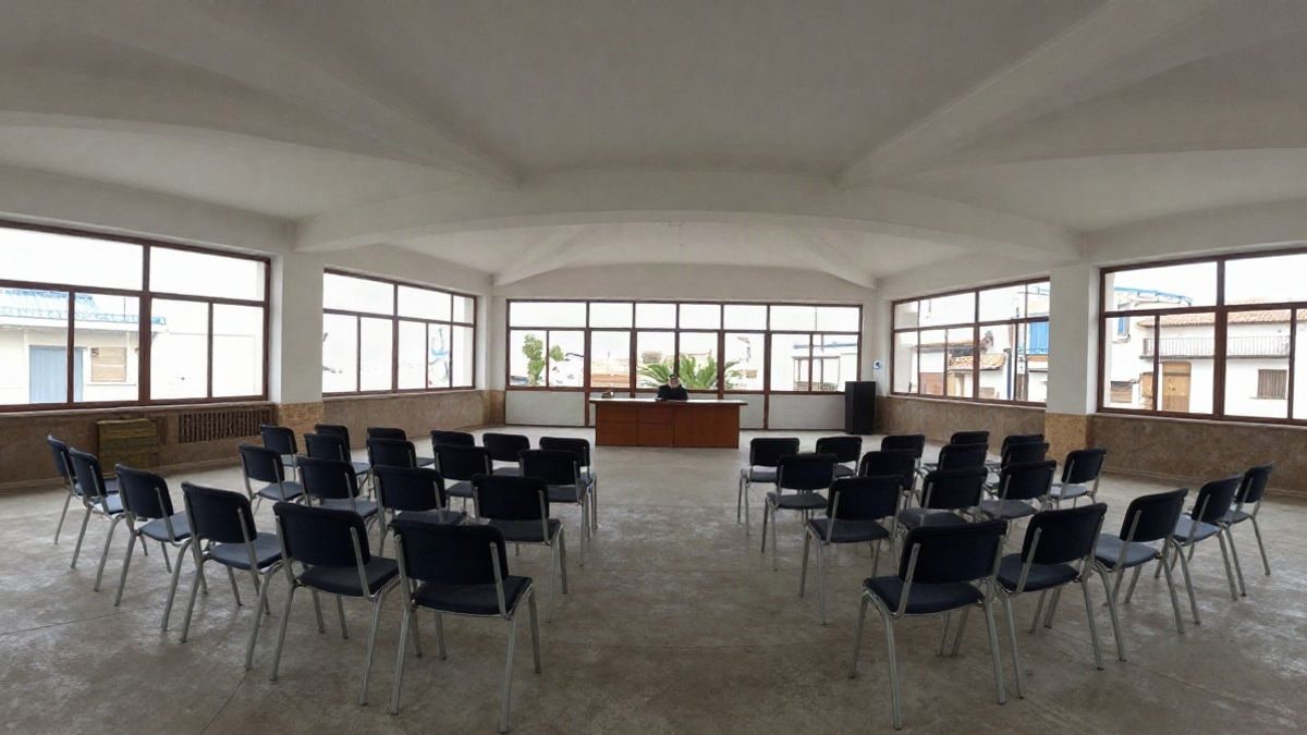 Imagen ilustrativa: sala de un centro cultural con sillas vacías y mesa de ponentes