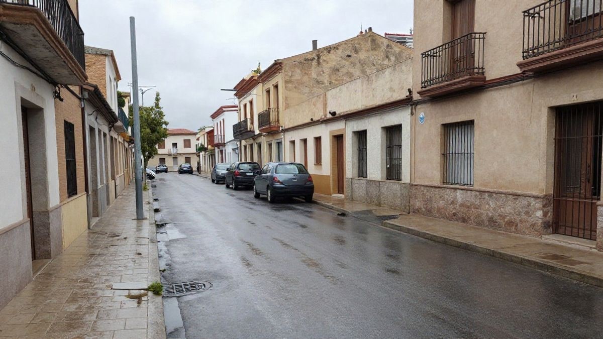 Imagen ilustrativa: calle de Barcelona con el asfalto mojado y el cielo gris, con imbornales visibles y coches aparcados