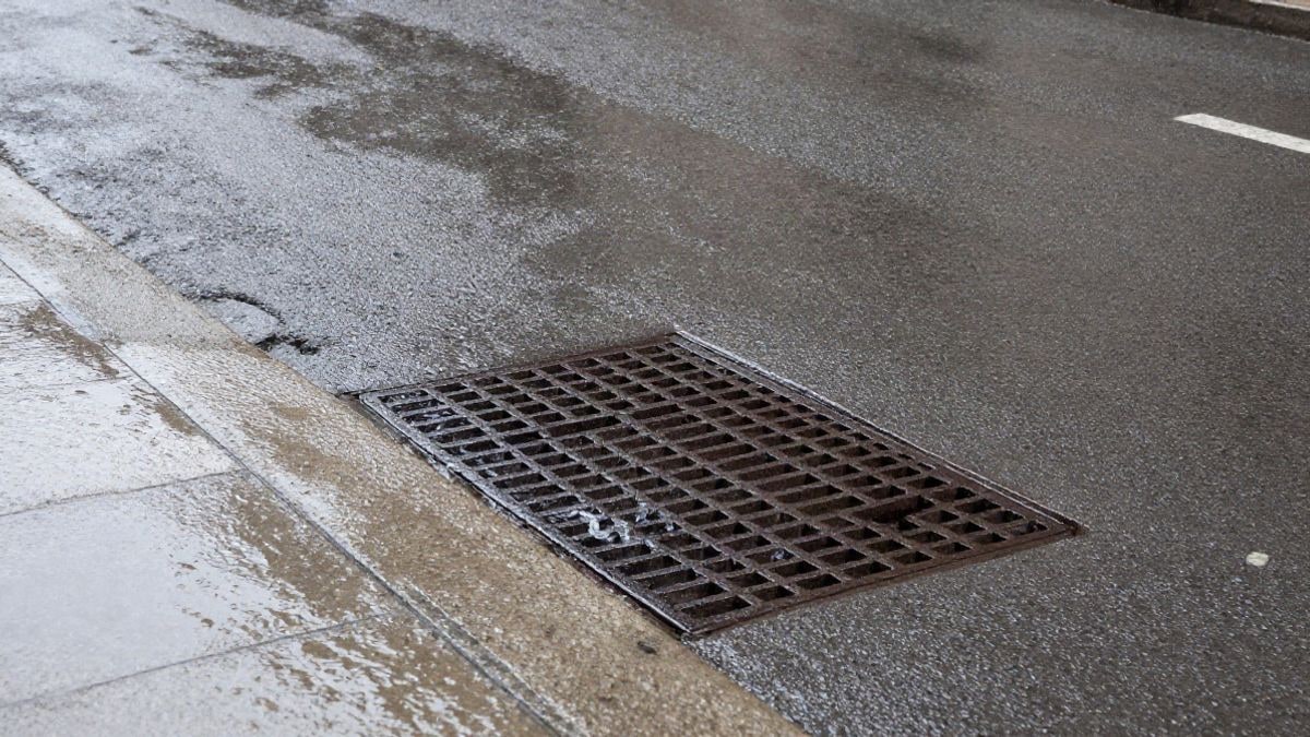 Imagen ilustrativa: detalle de asfalto mojado y una rejilla de alcantarillado con agua de lluvia