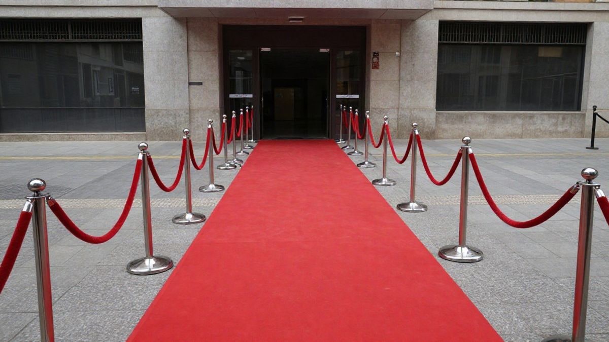 Imagen ilustrativa: gran angular de una alfombra roja con líneas convergentes hacia una fachada moderna, sin gente