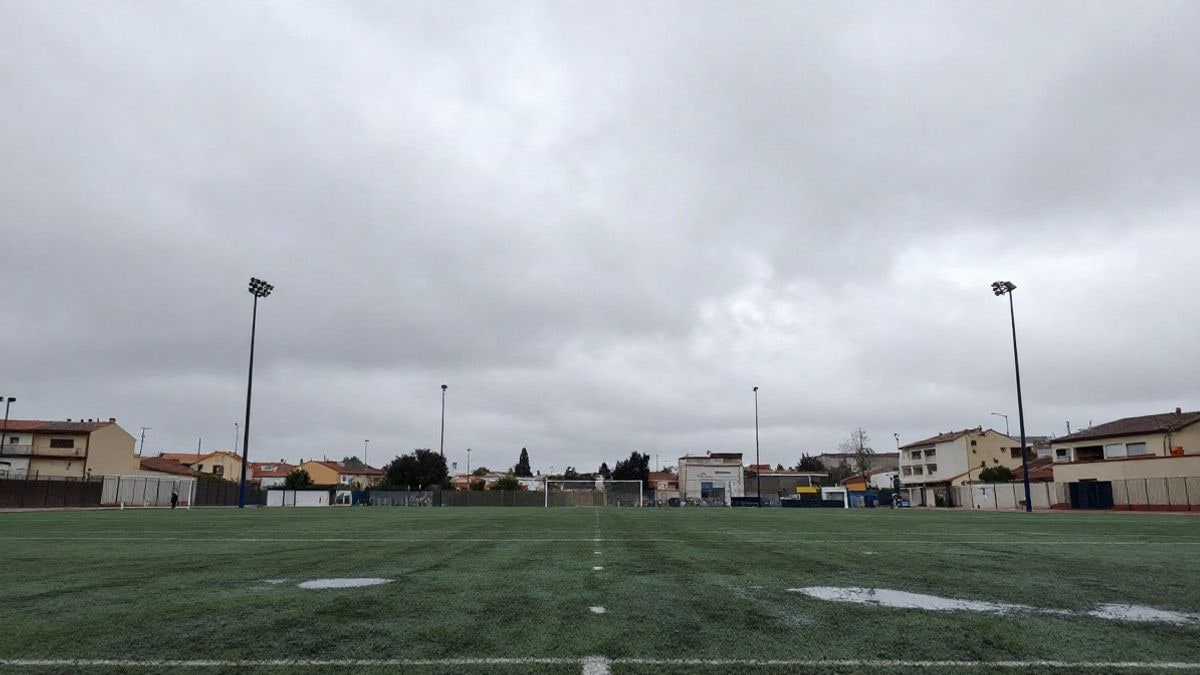 Imagen ilustrativa: campo deportivo vacío bajo un cielo gris con charcos de lluvia