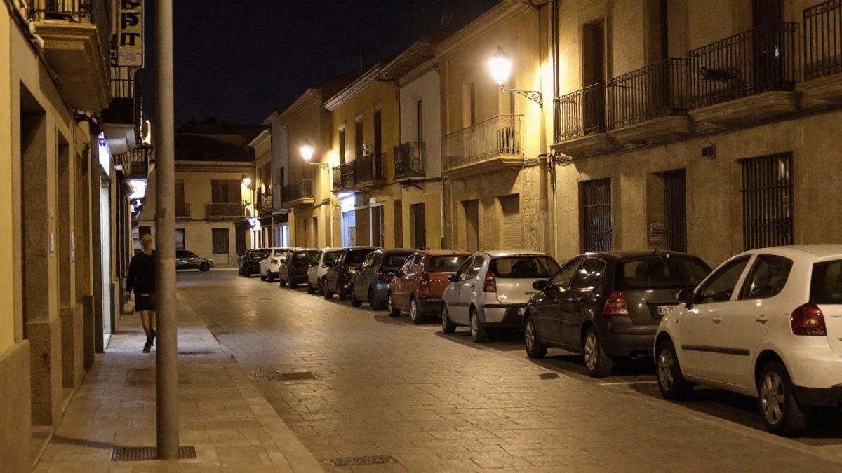 Imagen ilustrativa: calle corriente de noche iluminada por farolas y un letrero tenue, sin personas visibles