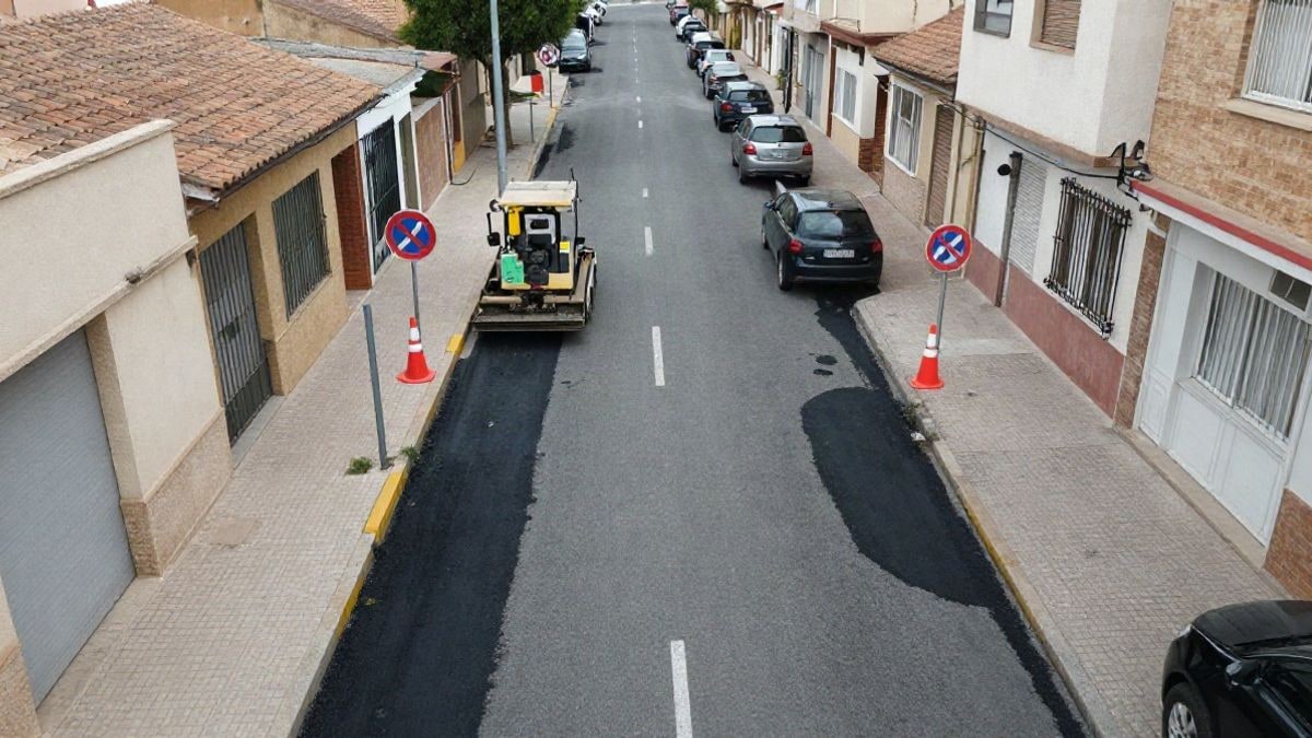 Imagen ilustrativa: vista cenital de una calle residencial con parches de asfalto nuevo, conos y señal de prohibido aparcar