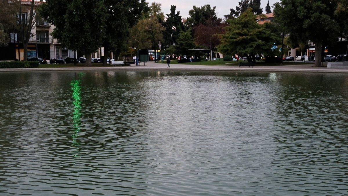 Imagen ilustrativa: un lago de un parque público iluminado de verde al anochecer, con reflejos en el agua