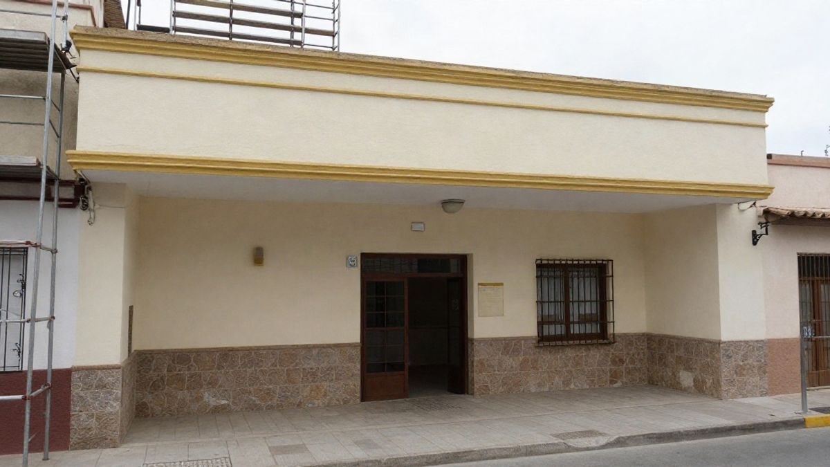 Imagen ilustrativa: fachada de una escuela pública con la cornisa recién pintada y andamios retirados parcialmente, bajo un cielo nublado.