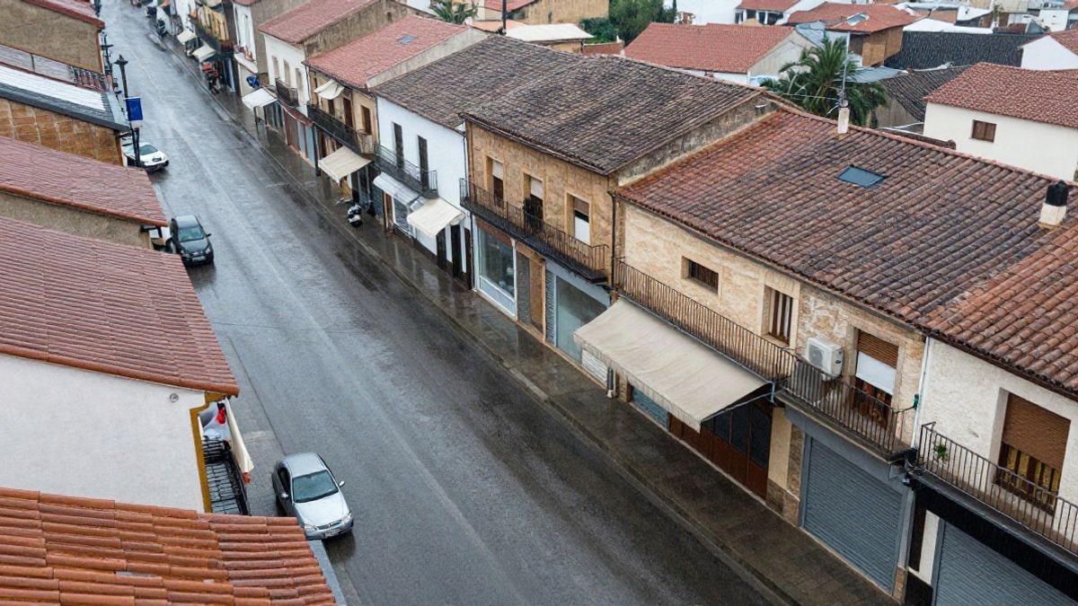 Imagen ilustrativa: vista cenital de una calle de pueblo bajo la lluvia con asfalto mojado y charcos
