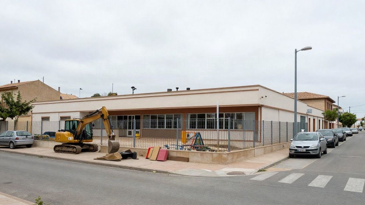 Imagen ilustrativa: edificio escolar de obra con valla de construcción y materiales en una calle de pueblo