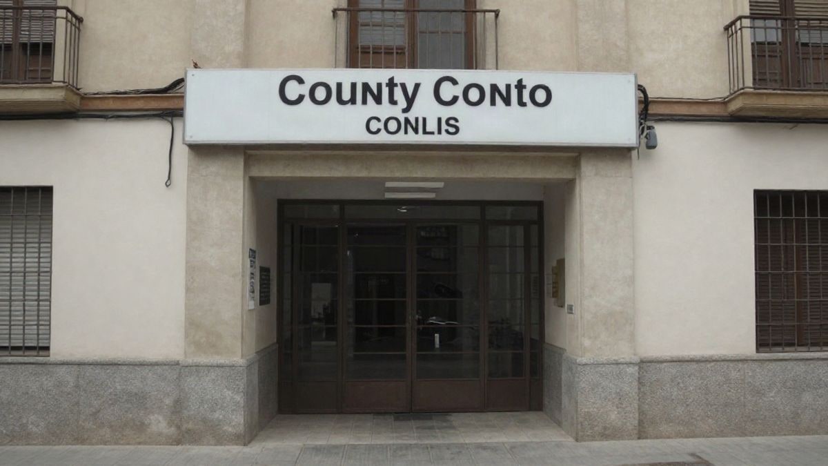 Imagen ilustrativa: entrada de un edificio institucional con un cartel informativo en una calle corriente