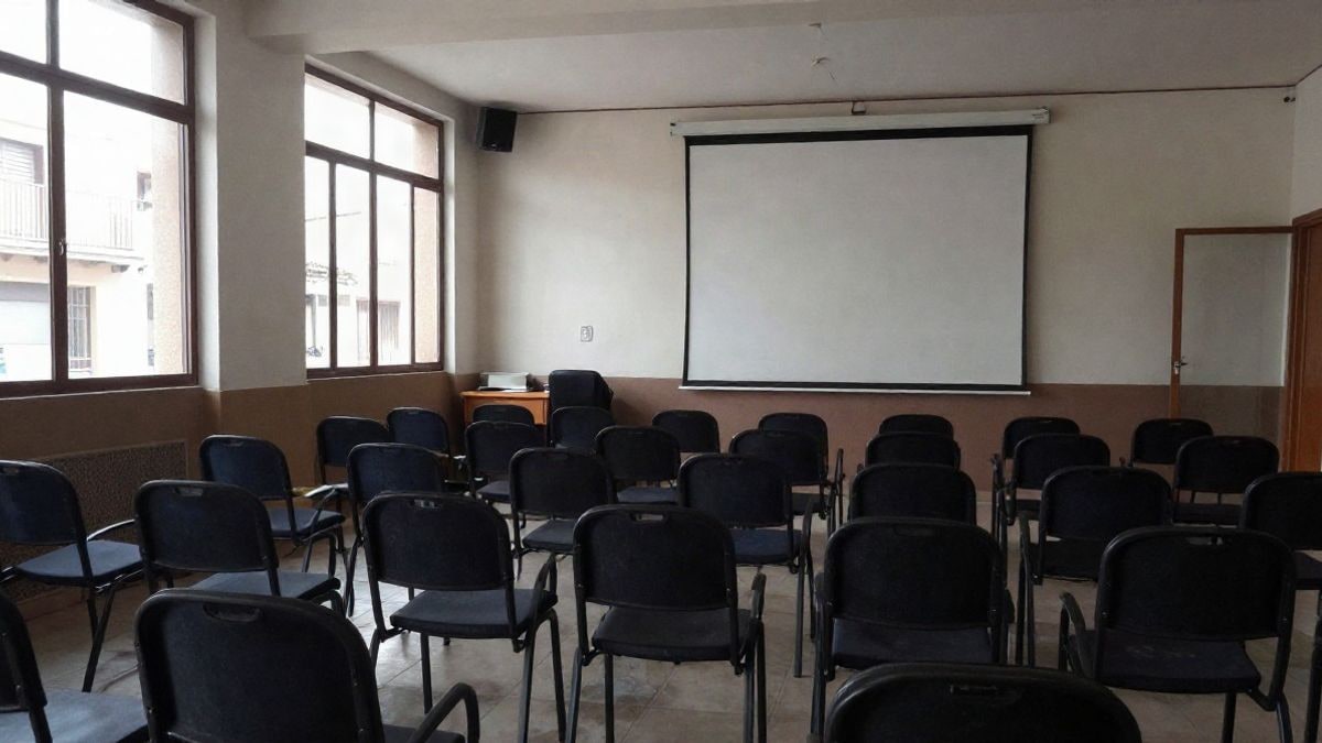 Imagen ilustrativa: interior de una sala de reuniones con sillas vacías y una pantalla de proyección, iluminada por luz lateral de ventana