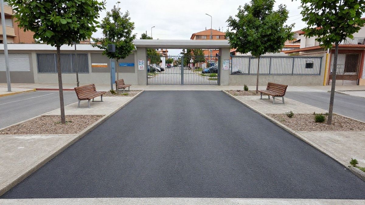 Imagen ilustrativa: acera recién urbanizada con bancos y árboles junto a la entrada de un centro escolar genérico