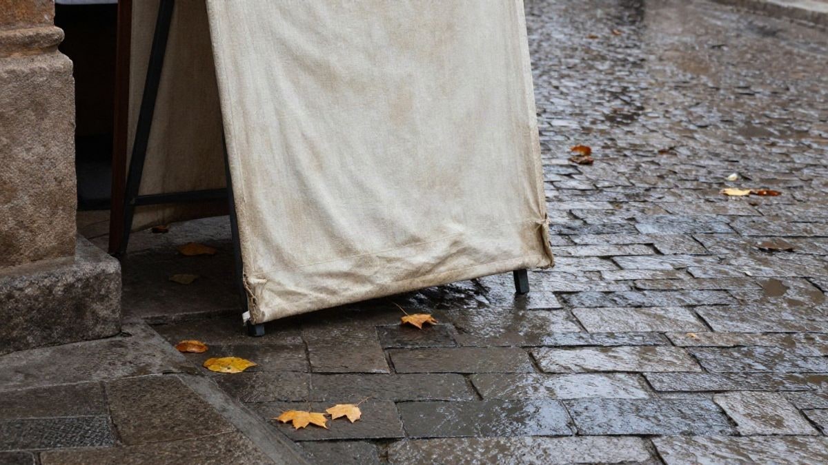 Imagen ilustrativa: detalle de adoquines mojados y lona de puesto de mercado plegada tras la lluvia