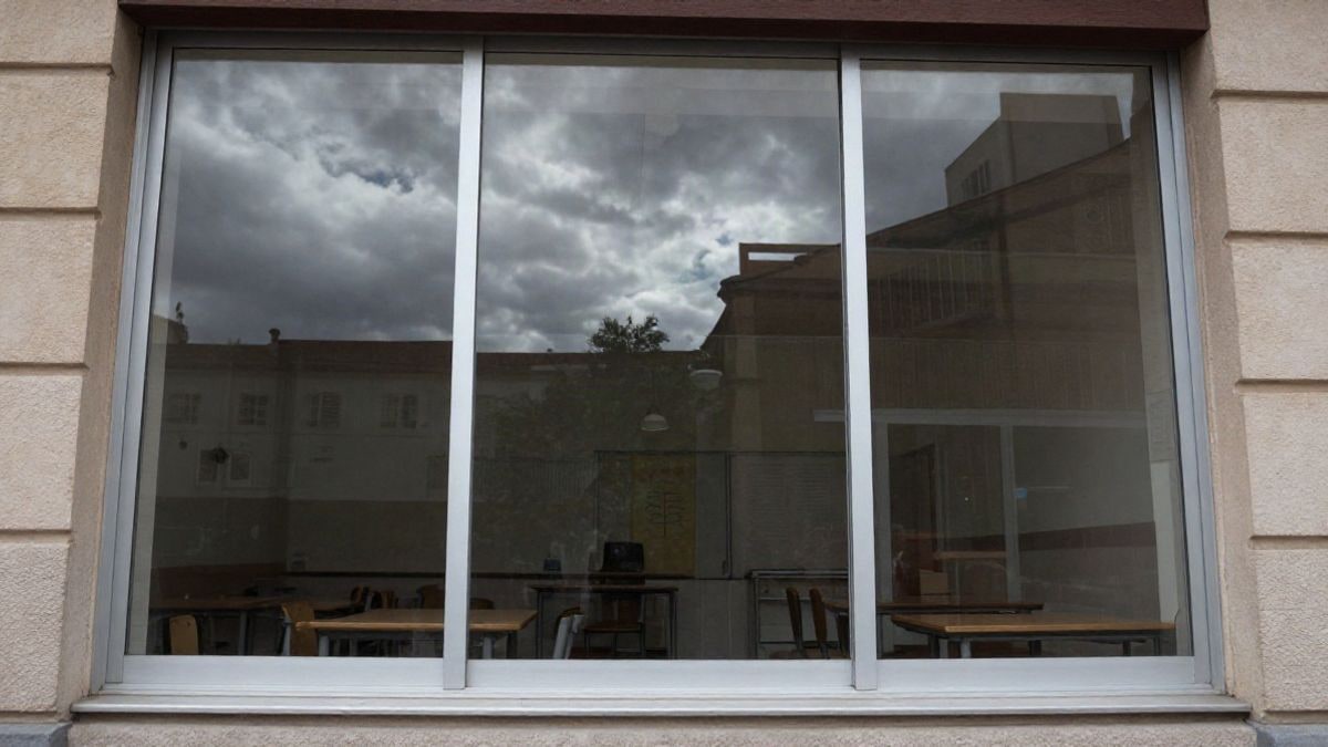 Imagen ilustrativa: aula vacía con sillas y mesa, vista desde el suelo con cielo nublado al fondo