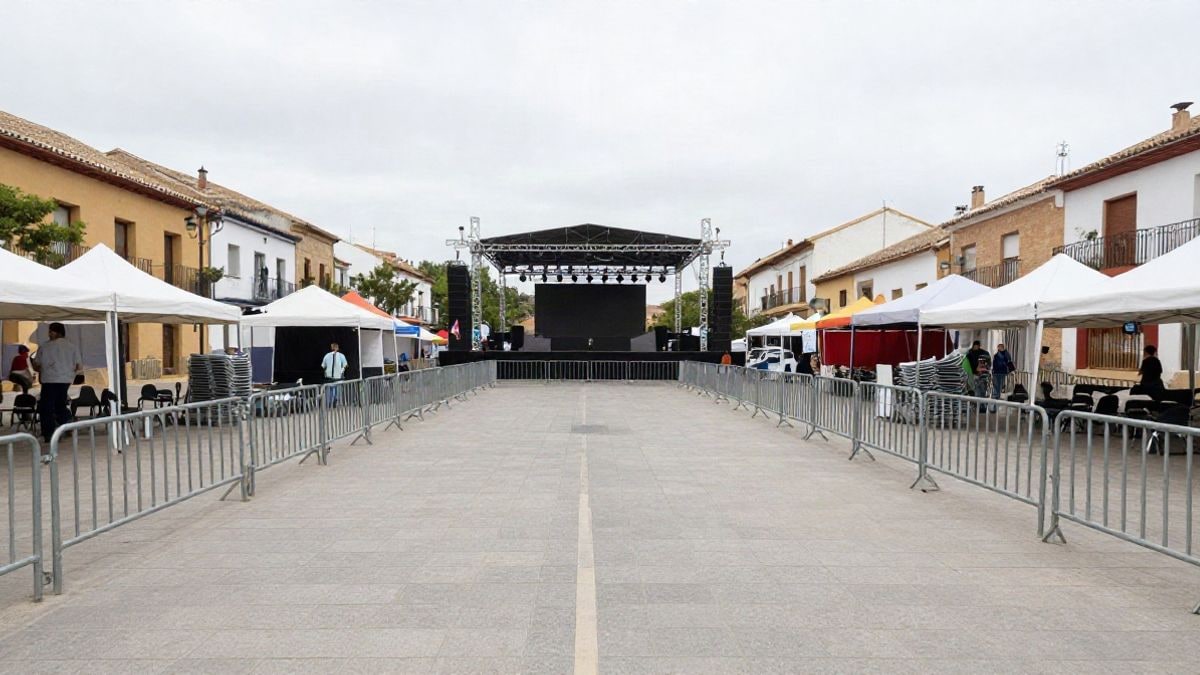 Imagen ilustrativa: recinto genérico de fiesta mayor con escenario y vallas metálicas vistas en gran angular