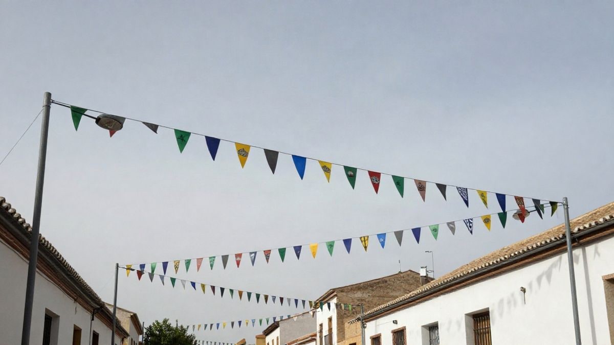 Imagen ilustrativa: banderines de fiesta mayor colgados entre farolas en una calle residencial, vistos desde el suelo con el cielo al fondo