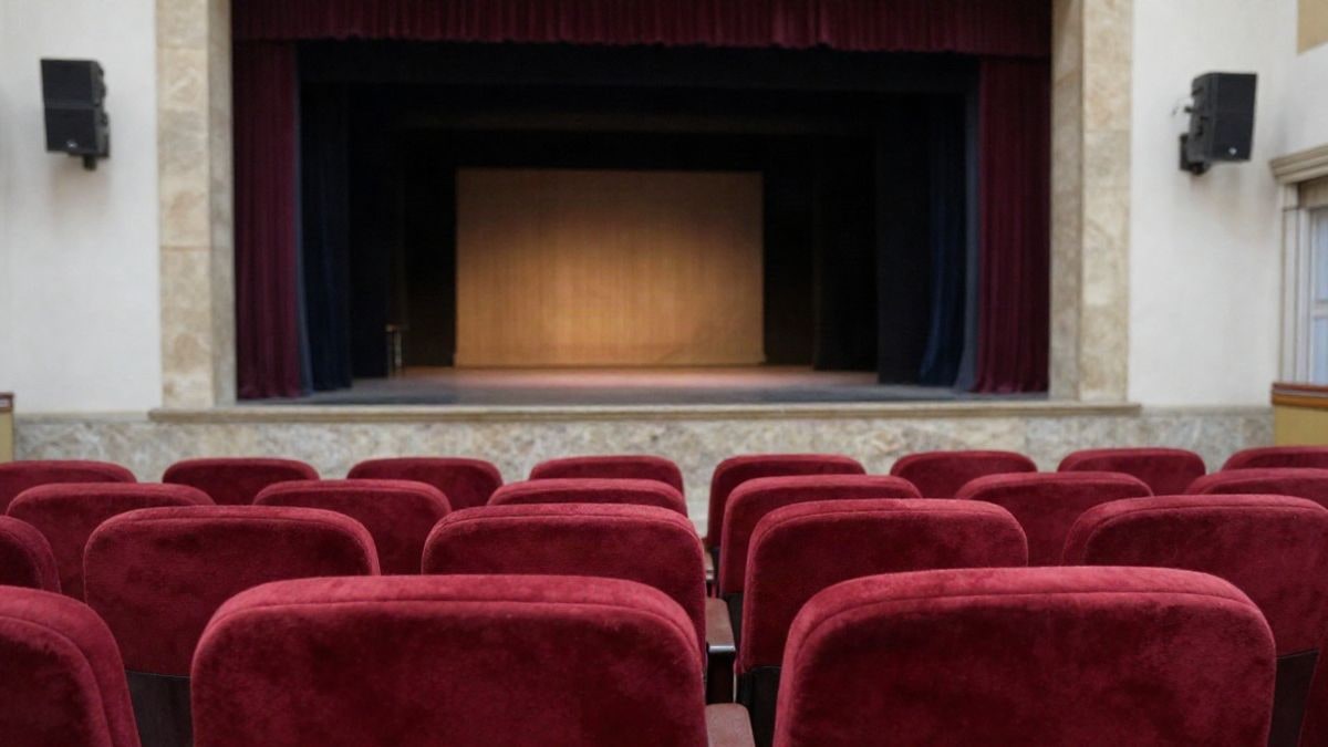 Imagen ilustrativa: vista lateral de un escenario de teatro con butacas rojas vacías en primer plano