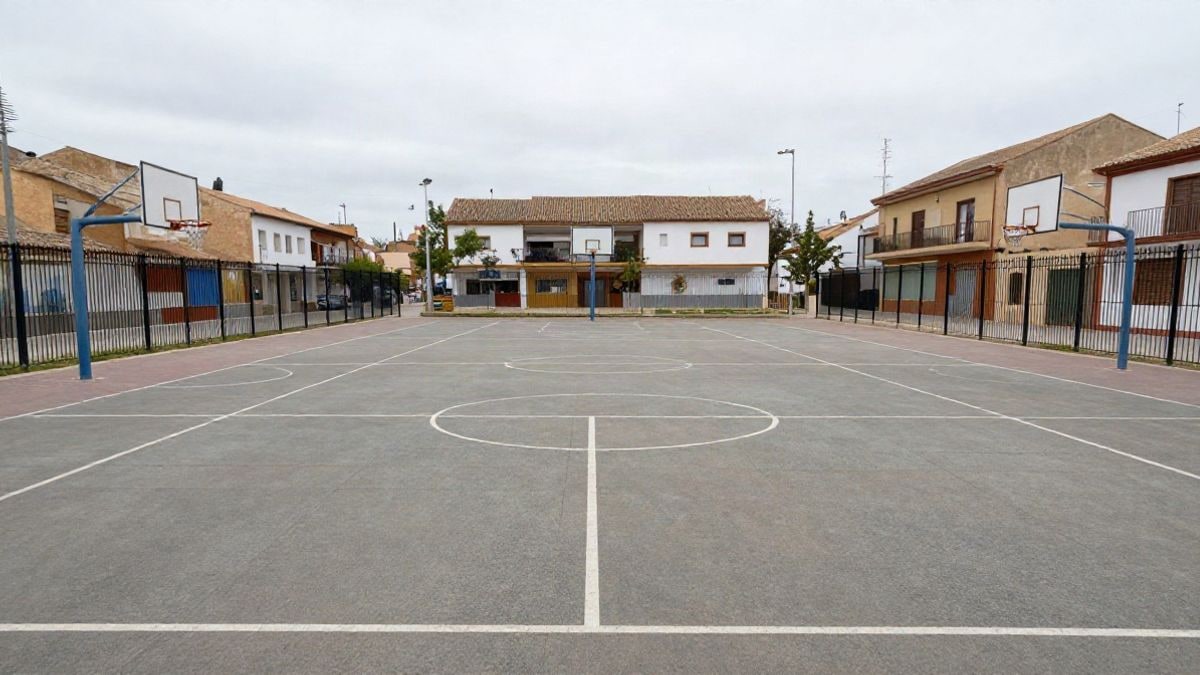 Imagen ilustrativa: patio de una escuela con pista deportiva y canastas, sin personas, en un día nublado.
