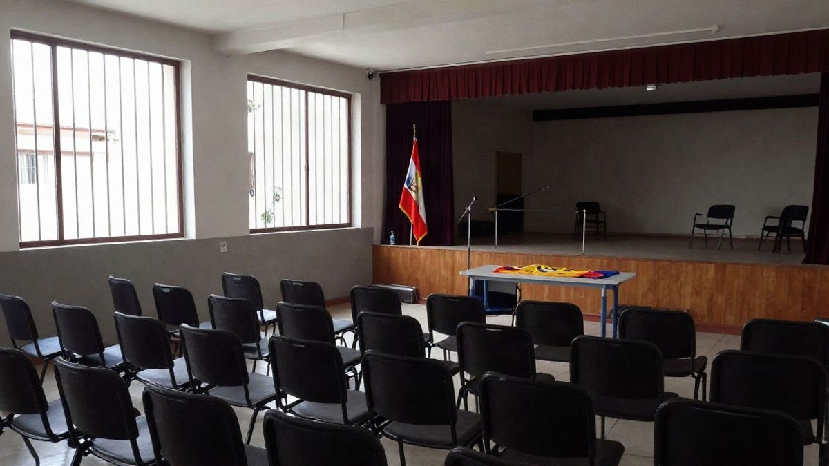 Imagen ilustrativa: interior de una sala con sillas vacías y un atril preparado para un acto cultural