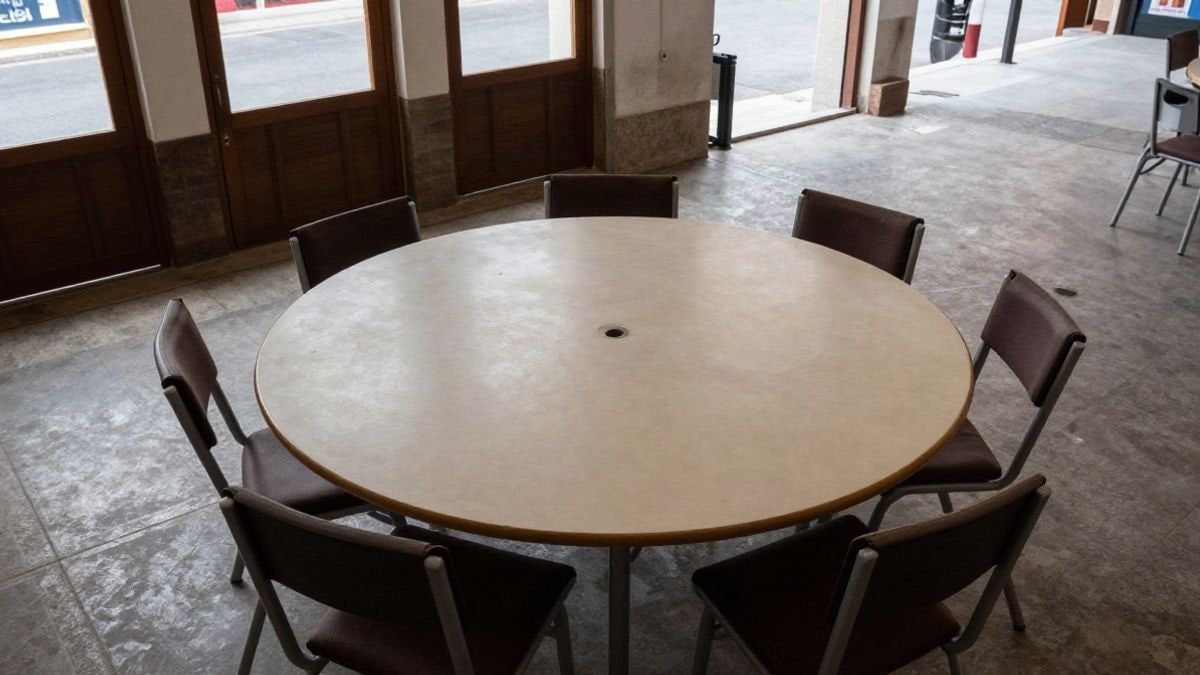Imagen ilustrativa: vista cenital de una mesa redonda vacía con sillas en una sala comunitaria