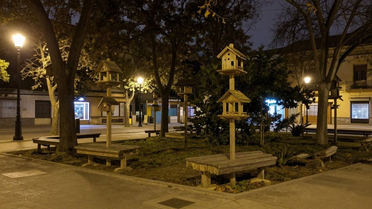 Imagen ilustrativa: comederos y refugios para pájaros colgados en un parque iluminado por farolas