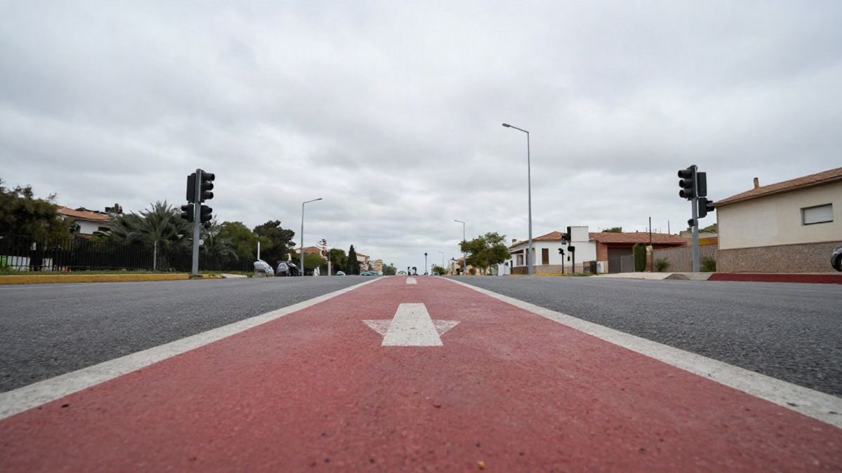 Imagen ilustrativa: ángulo bajo de un cruce urbano genérico con carril pintado de rojo y cielo nublado