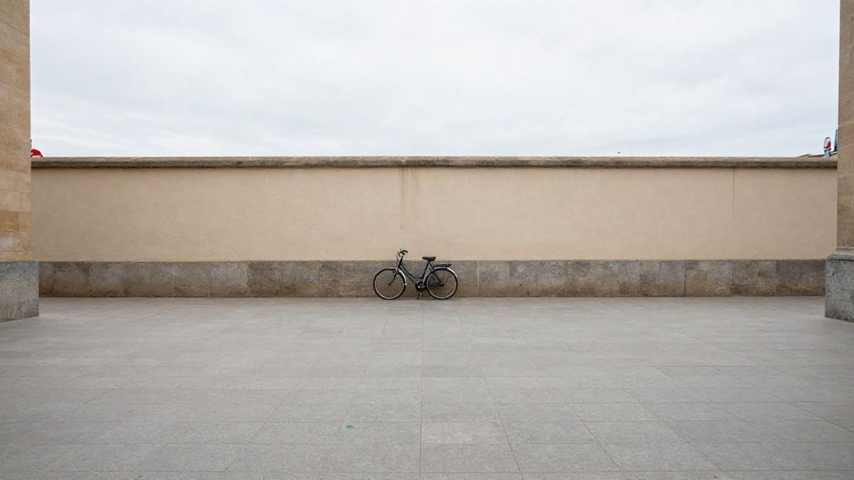 Imagen ilustrativa: una bicicleta apoyada en una pared de una plaza urbana vacía, con una parada de bus al fondo