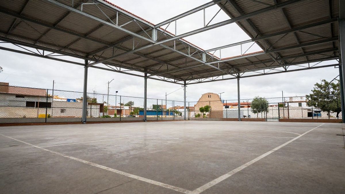 Imagen ilustrativa: cancha de baloncesto escolar vacía con estructura de cubierta metálica en un patio