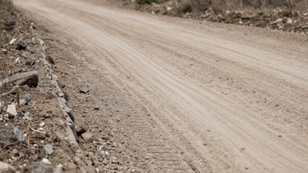 Imagen ilustrativa: camino rural de tierra con grava compactada y una pequeña cuneta de drenaje en el borde