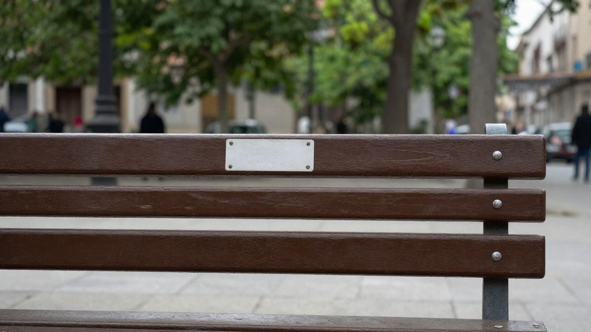 Imagen ilustrativa: banco de madera en un parque público con un cartel genérico, sin texto legible