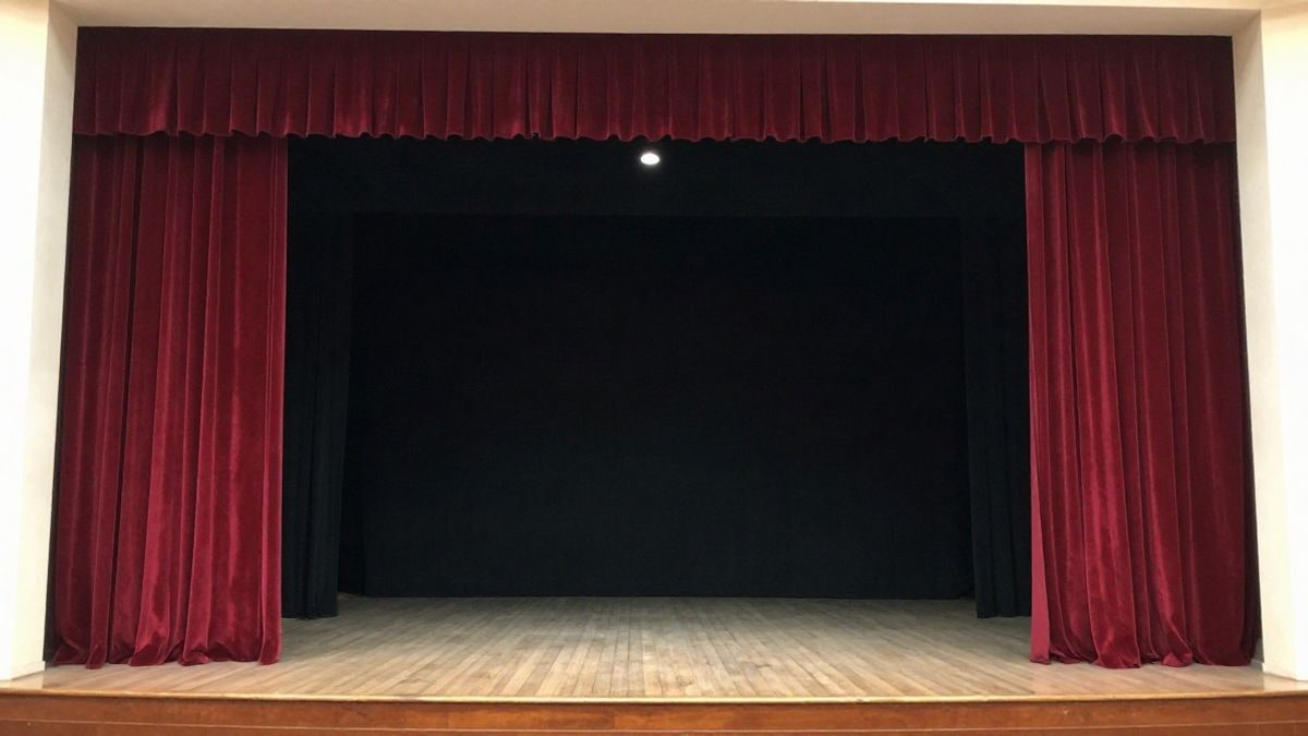 Imagen ilustrativa: un escenario teatral vacío con telón rojo y un foco encendido, listo para una nueva función.