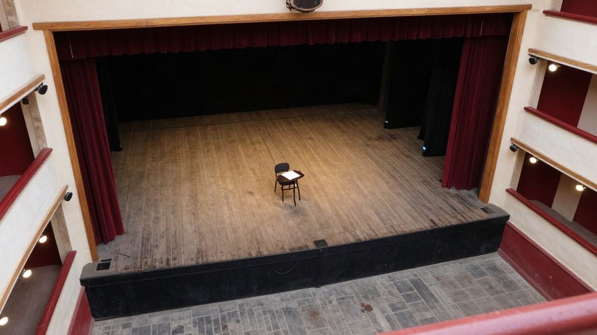 Imagen ilustrativa: vista cenital de un escenario de teatro vacío con una silla y un guion sobre una mesa